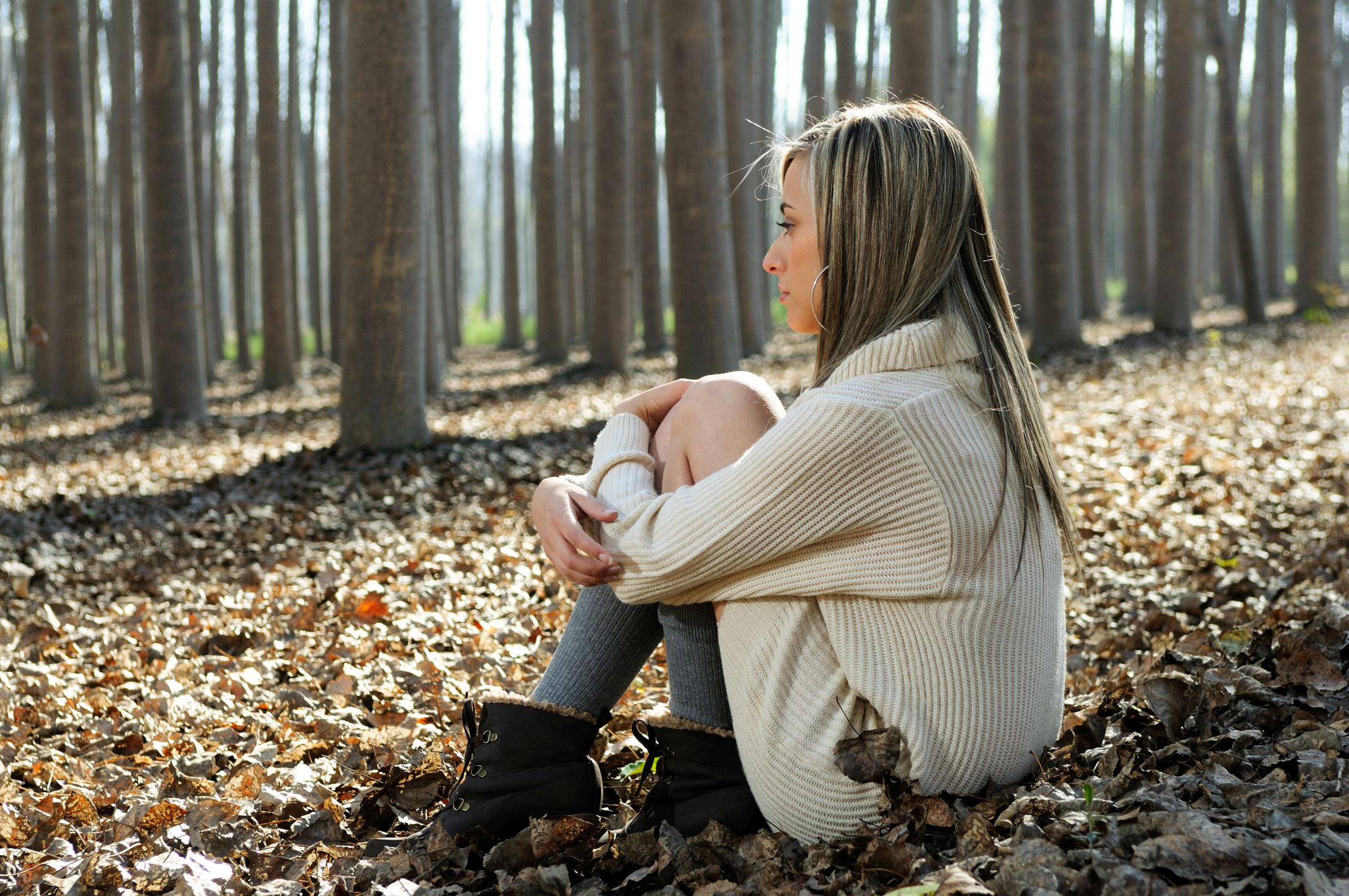 Beautiful blonde sitting on leaves in a forest of poplars